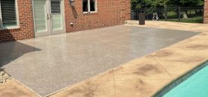 Outdoor epoxy-coated patio beside a pool with brick house and concrete seating area